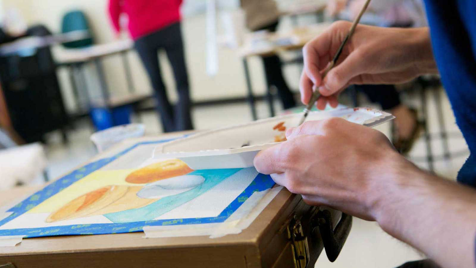 Photo of a watercolor still-life painting, painters palette and student holding a paintbrush