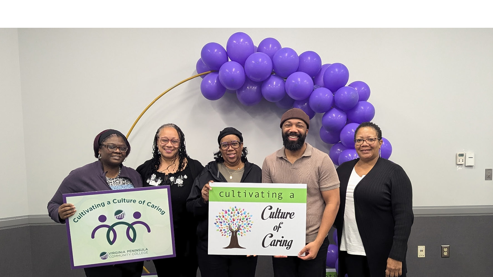 Feature image for the page. Photo of VPCC staff posing in front of purple balloons and holding up signs for the "Culture of Caring".
